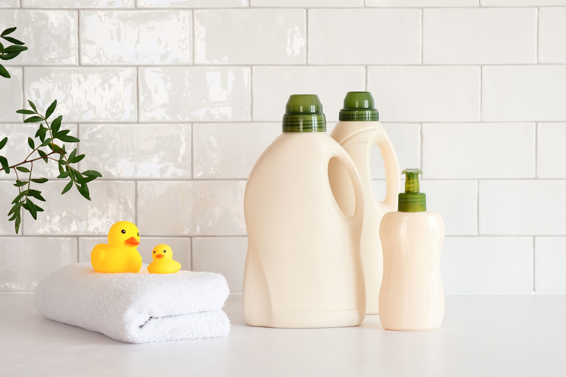 Eco friendly organic natural baby laundry detergent and soap gel bottle with branch of green leaves, towel and yellow duck on table in bathroom. Baby hygiene products packaging design, branding.